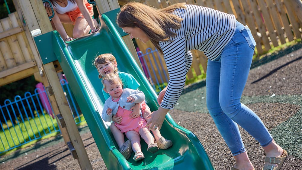A mother catching her kids coming down a slide in a playground