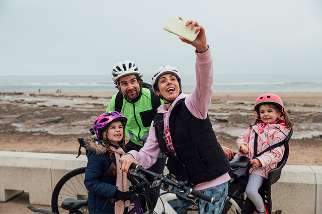 A family taking a selfie while cycling by the beach