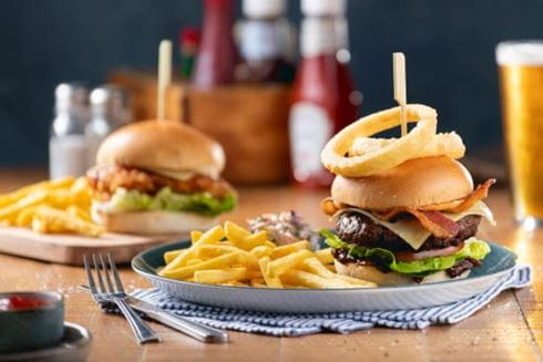 Burger stacked with onion rings with a side of fries