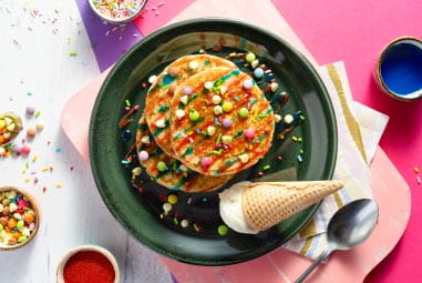 Pancakes topped with colourful sprinkles and an ice cream cone on the side
