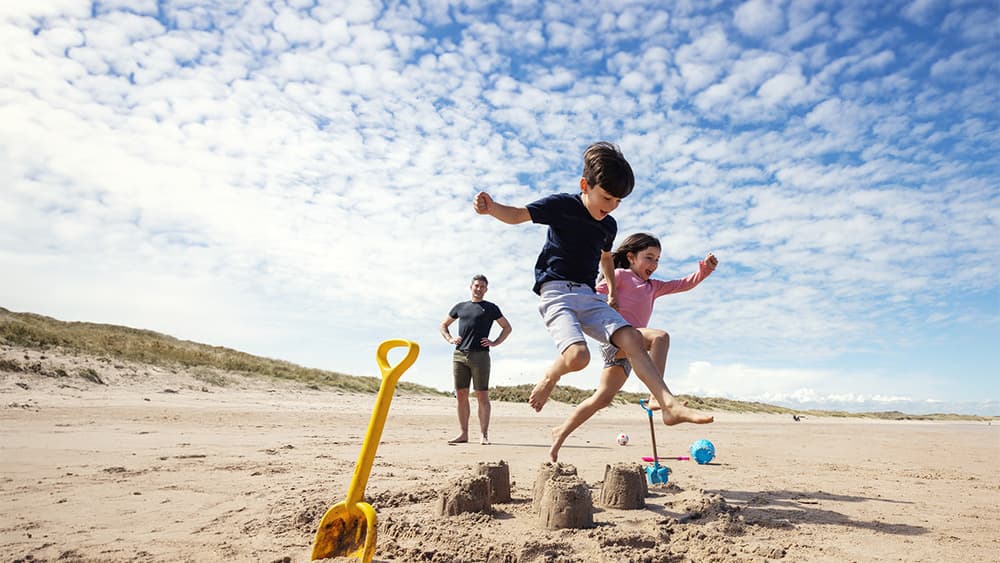 Children jumping over a sandcastle at the beach