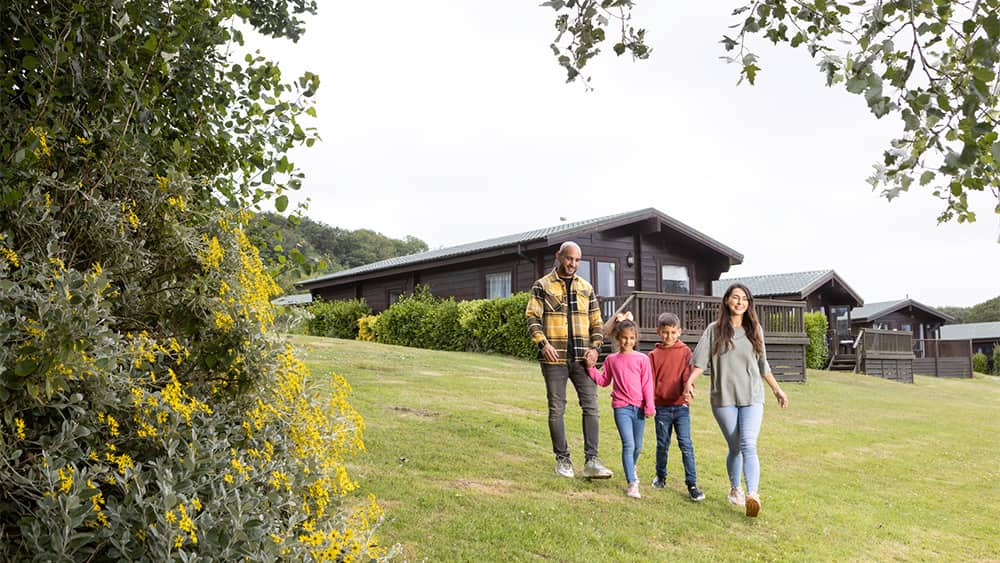 A family walking past their lodge at White Acres Holiday Park in Cornwall