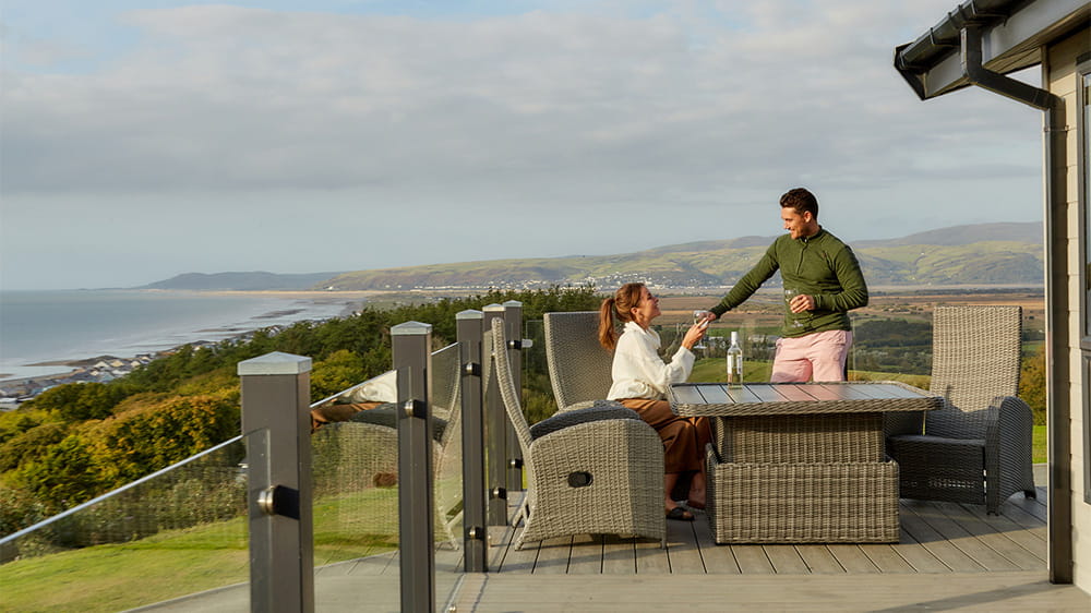 A couple enjoying a drink on their lodge's veranda at Brynowen Holiday Park in Wales