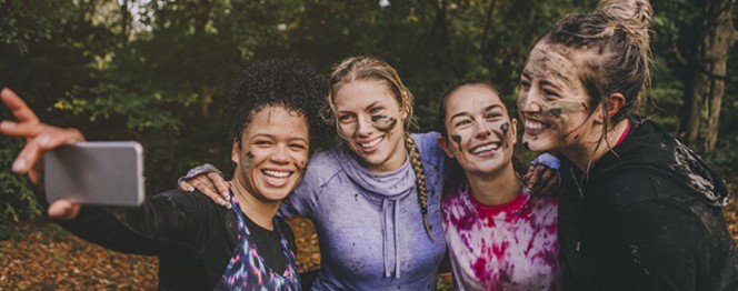 Four teenage girls with facepaint on taking a selfie in a forest