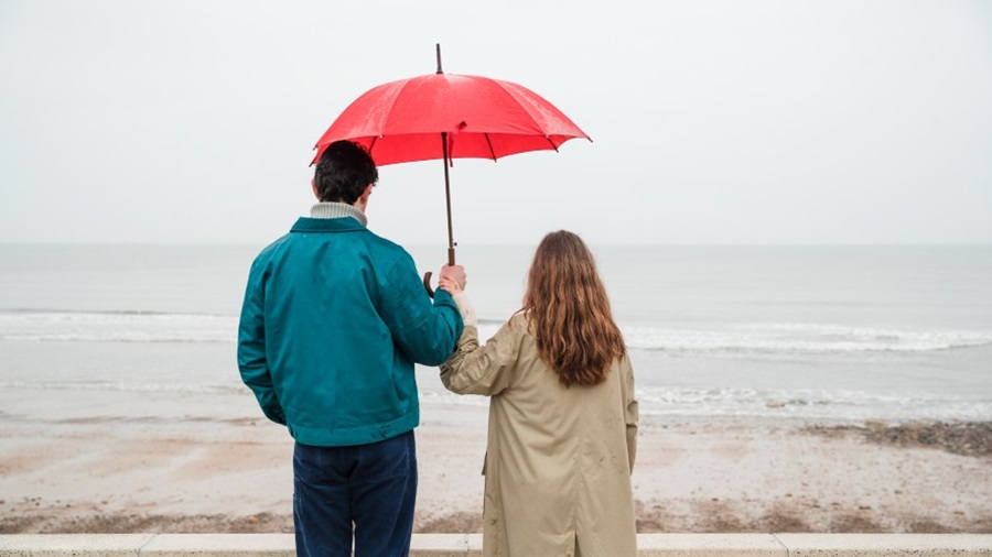 A couple standing on a beach holding an umbrella looking out to sea