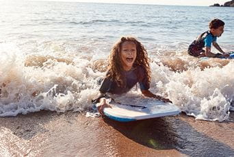 Two children bodyboarding on a UK beach