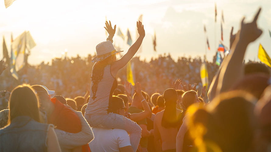 A crowd of concert goers enjoying a festival at sunset
