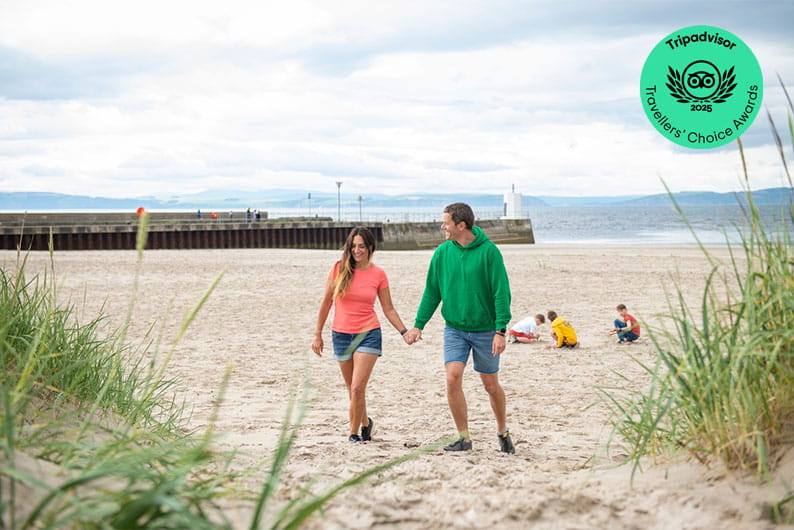 A couple walking along the beach by Nairn Lochloy Holiday Park in Scotland