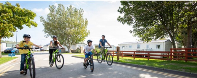 A family riding bikes around Ty Mawr Holiday Park on a sunny day