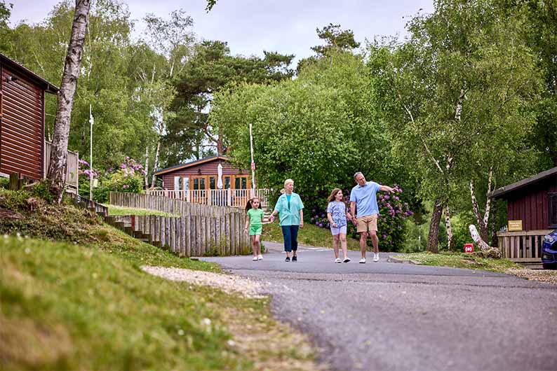A family walking past woodland lodges at Warmwell Holiday Park