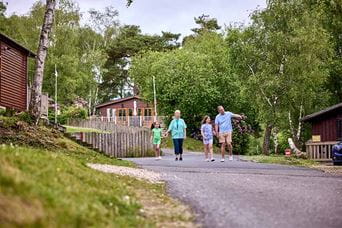 A family walking past woodland lodges at Warmwell Holiday Park