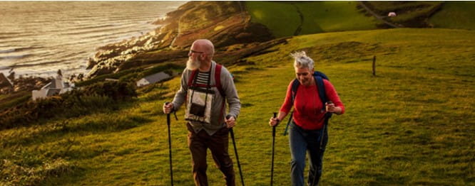 an elderly couple walking through a field next to the sea