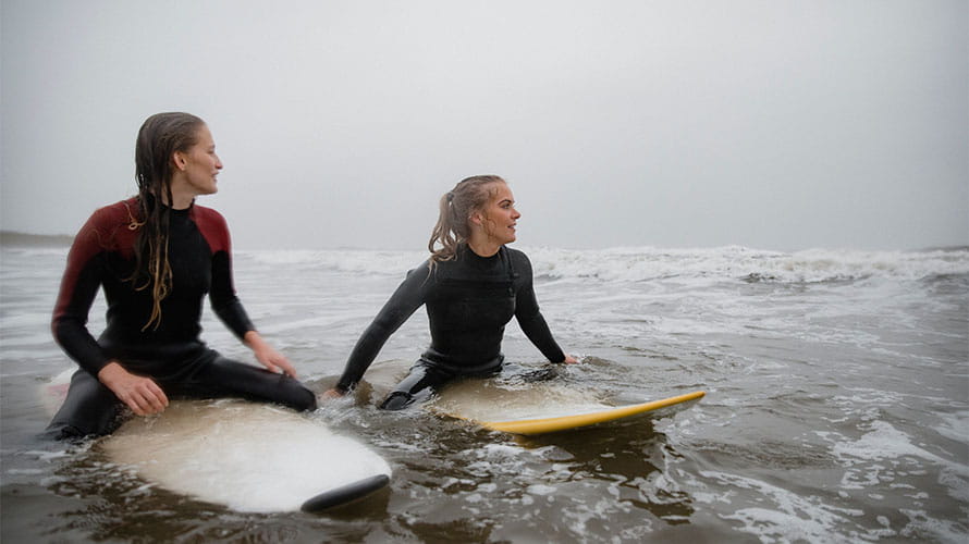 Friends sitting on surf boards in the sea on a rainy day