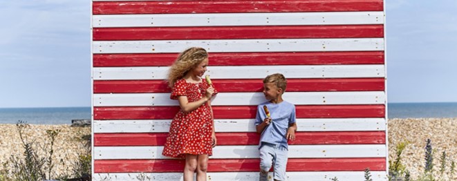 Two children eating ice lollies in front of beach huts by the sea at Romney Sands