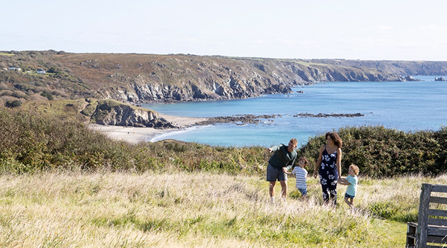A family walking across a grassy area of Sea Acres Holiday Park with the sea in the background