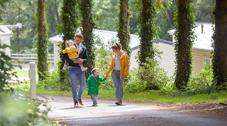 Parents and young children walking through the trees on Looe Bay Holiday Park