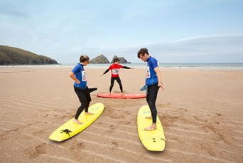 A couple taking a surfing lesson on Holywell Bay Beach in Cornwall