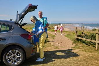 Granparents unpacking the car while their grandchildren run down to the beach