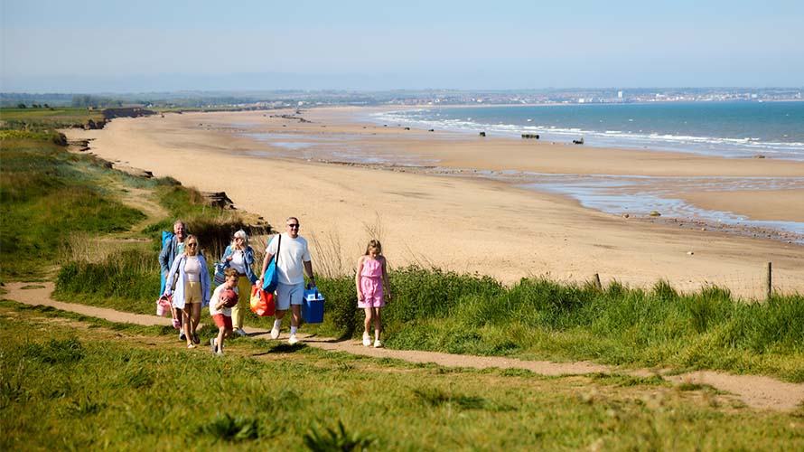 A family walking along a coastal path beside the beach