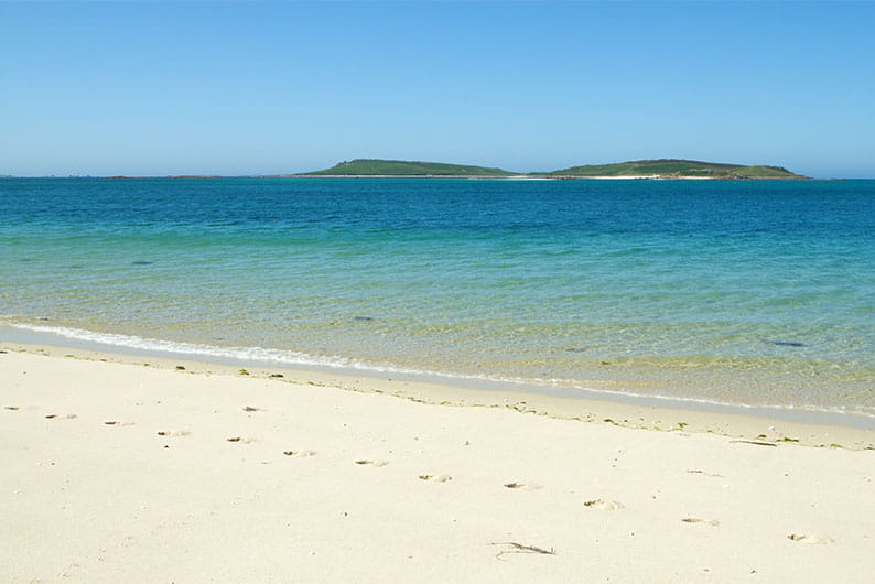 White sand and blue waters of Appletree Bay with the Scilly Isles in the distance