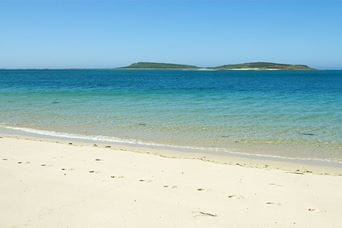 White sand and blue waters of Appletree Bay with the Scilly Isles in the distance