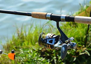 A fishing rod set up on the grass next to water