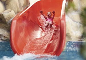 A child zooming down the waterslide into the indoor swimming pool