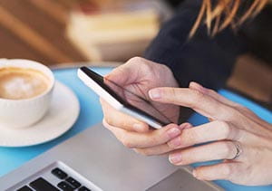 Someone using a mobile phone whilst enjoying a cup of coffee