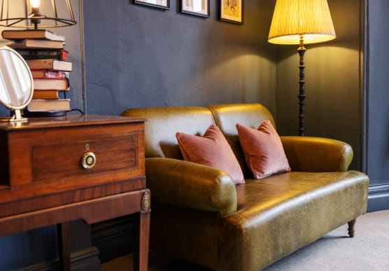 Green leather sofa with orange cushions and wooden console table