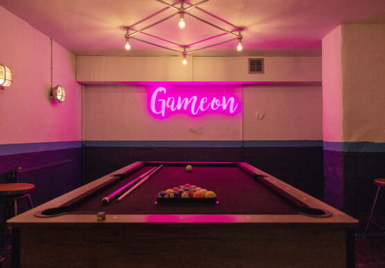Pool table with neon pink sign that read game on