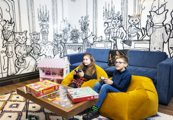 Little boy and girl sat on yellow bean bag playing a games console in a play room