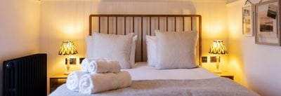 Neutral themed bedroom with double bed with metal frame headboard and rolled towels on the end