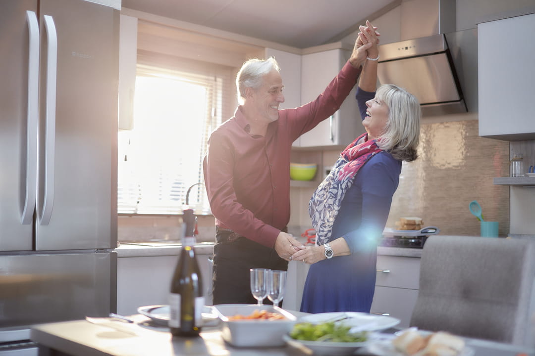 A couple dancing around the kitchen in their holiday caravan