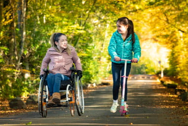 a woman in a wheelchair going down a lane with a child on a scooter