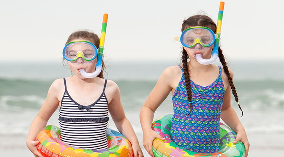 two girls at the sea shore wearing snorkels and rubber rings