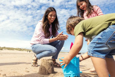 family with toddler building a sandcastle on the beach