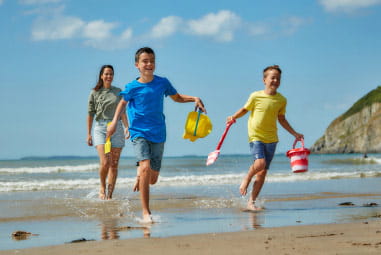 family running down a beach with buckets and spades