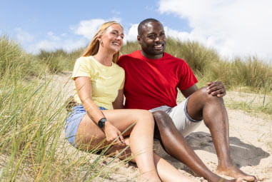 couple laughing together on a sand dune in the sunshine