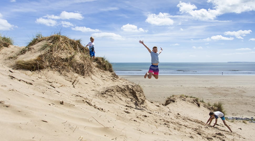three children playing on sand dunes and one child jumping off a sand dune