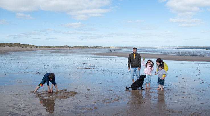 a family playing on the beach with a black dog