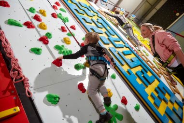 children on a climbing wall with parent watching
