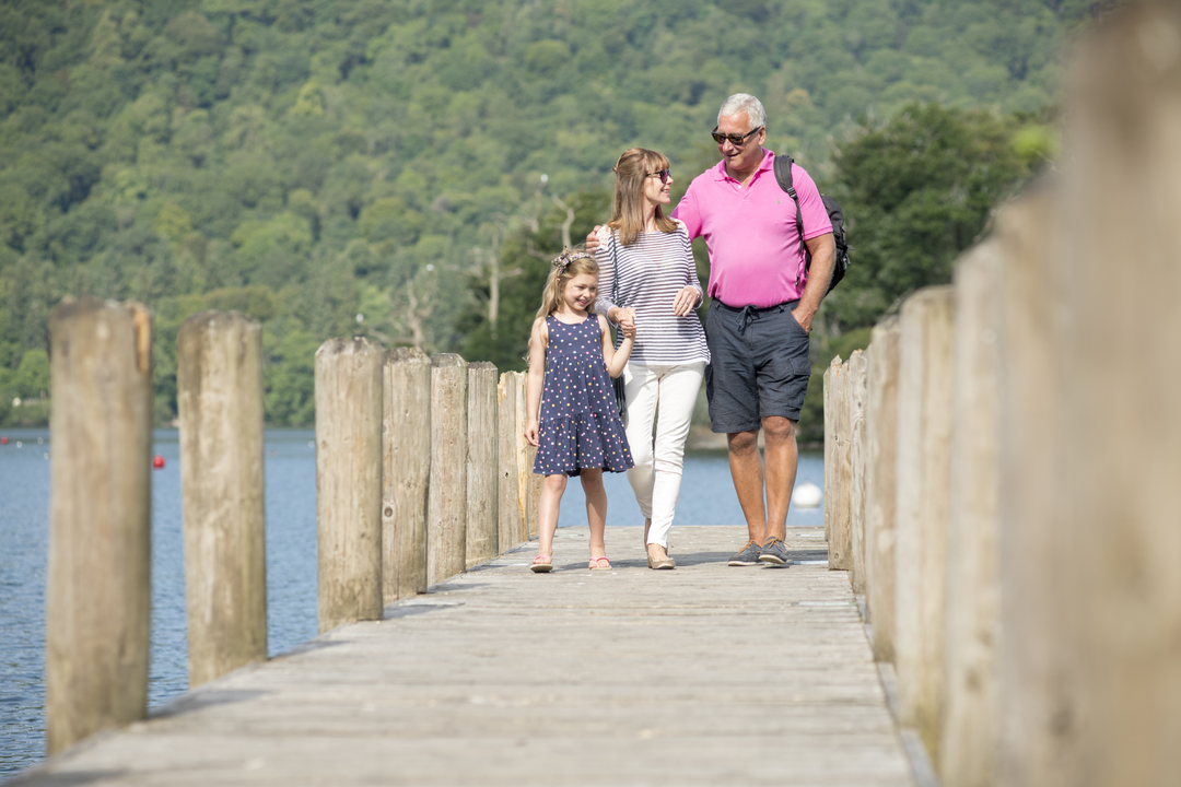 grandad mother and daughter walking along a pontoon on a lake