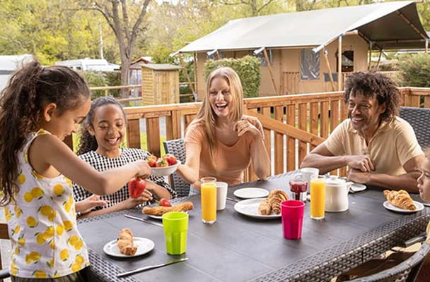 A family eating breakfast on the decking of their glamping safari tent