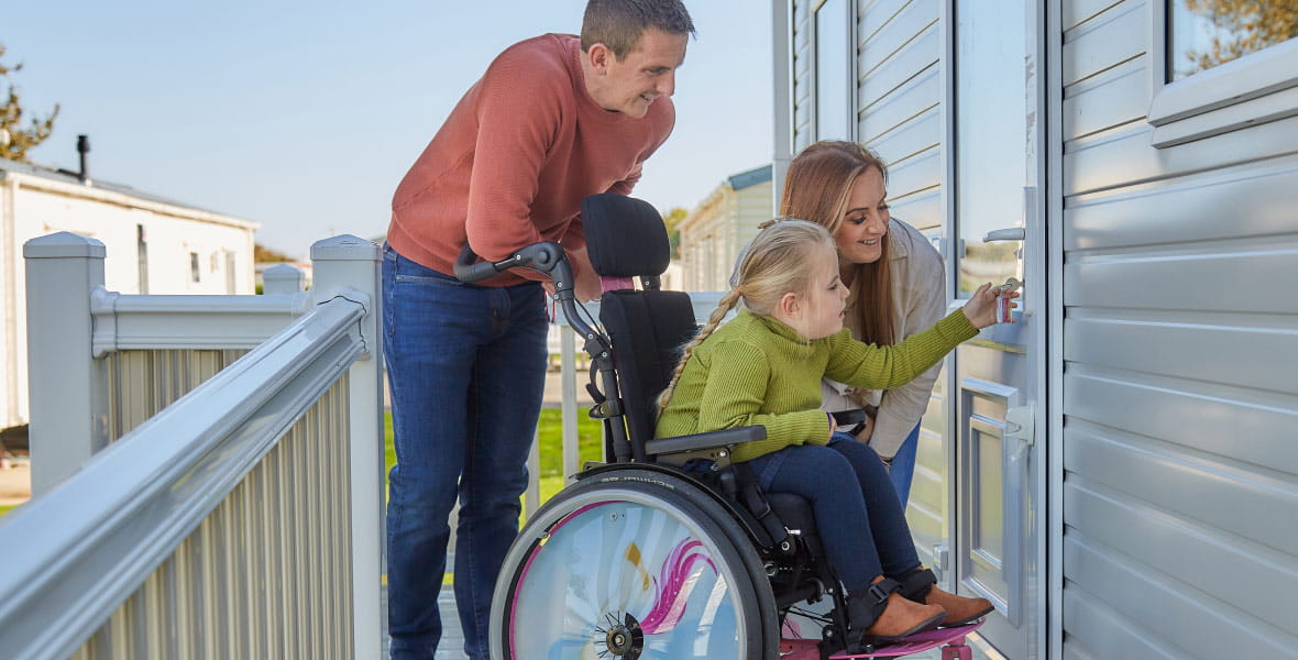 A young girl in a wheelchair with her family unlocks the door to their accessible caravan