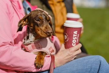 Person holding a dog and a coffee