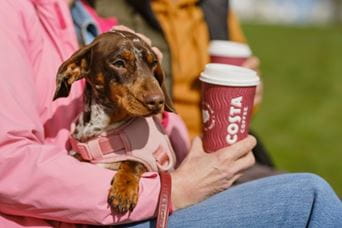 Person holding a dog and a coffee