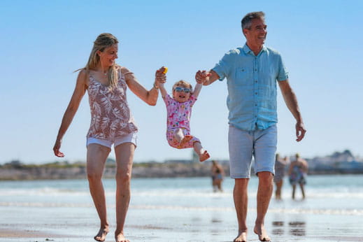 A couple strolling along a beach swinging their daughter in the air between them 