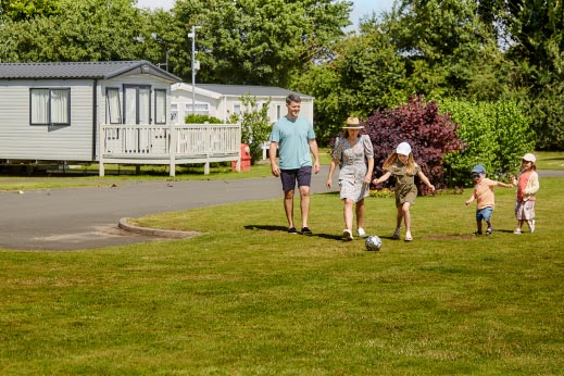 A family playing football outside a row of caravan holiday homes for sale