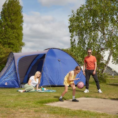 A family relaxing on the grass outside their tent on a Parkdean Resorts campsite
