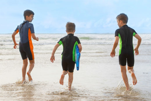 Boys running into the sea with surfboards